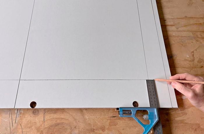 A person uses a combination square to measure and mark a cupboard side piece]