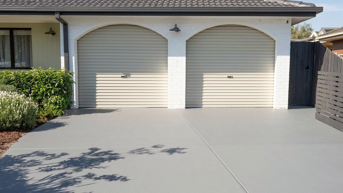 A freshly painted gray concrete driveway in front of a house with two garage doors.