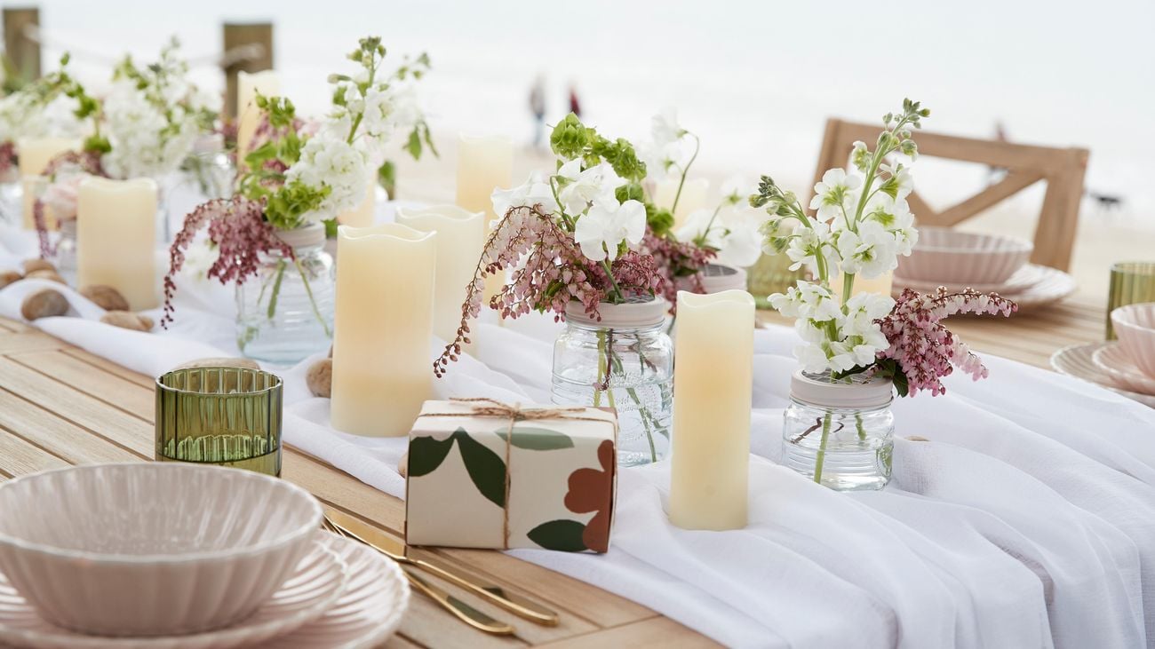 An outdoor table is decorated with a white tablecloth, candles and flowers