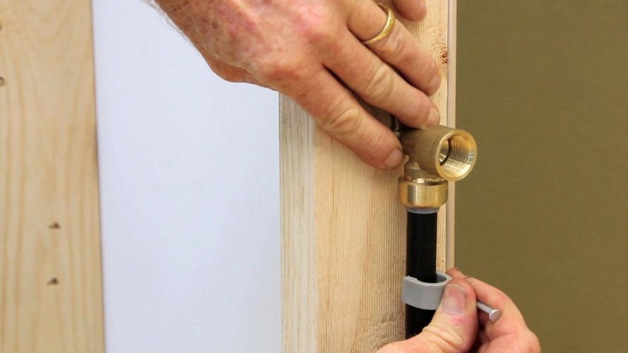 A person clipping a pipe to a wooden bar.