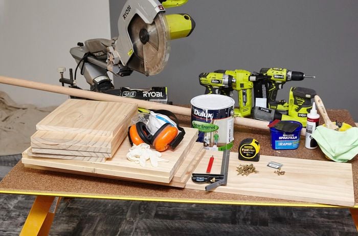 Tools and equipment for the job, including a mitre saw, several power drills, lengths of wood, paint, screws, wood glue, a piece of dowel, square rule and more