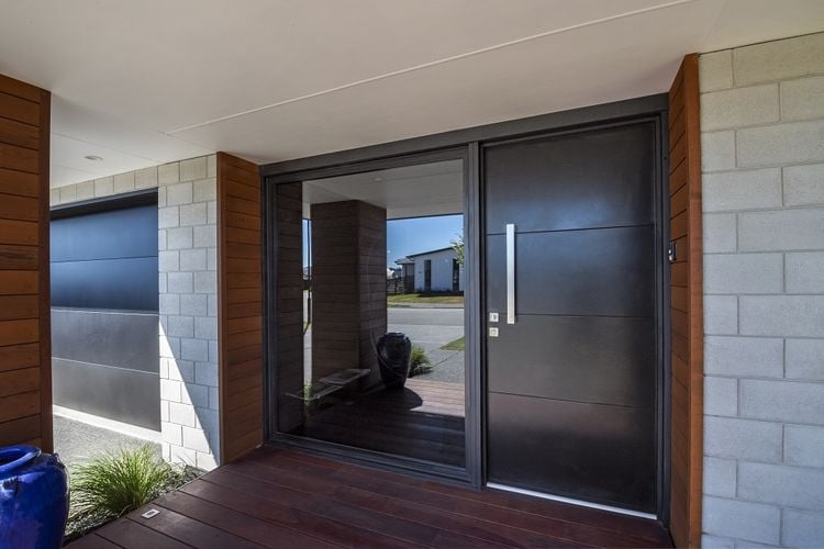 Covered entry to a grey brick house with a black front door
