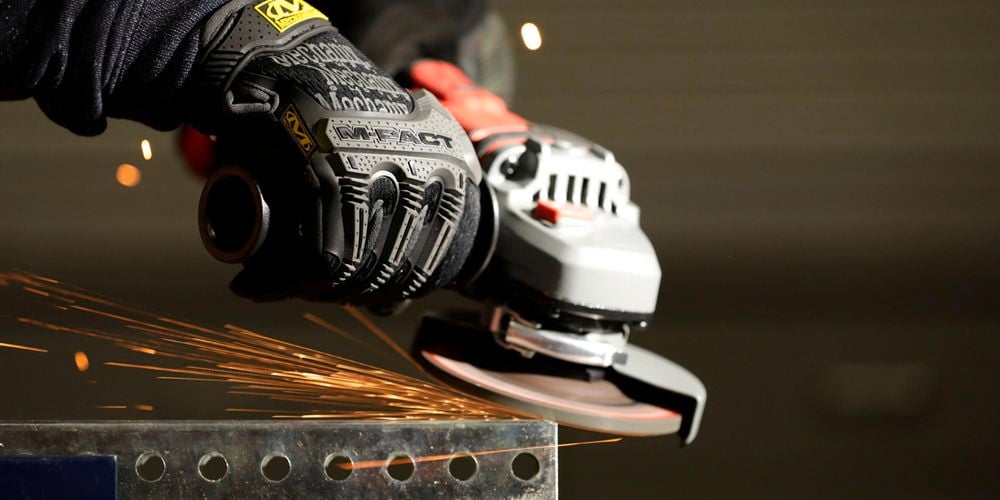 Close up of a person wearing protective gloves and using an angle grinder on a steel reinforcement.