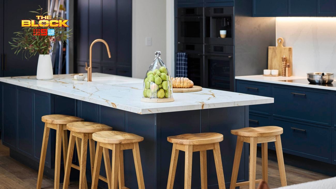 Kitchen island with marble top, gold faucet, and wooden stools.