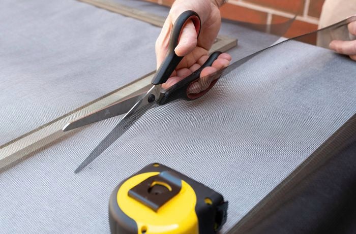 A person is cutting a flyscreen mesh to size using scissors along the marked measurements for a clean edge.  
