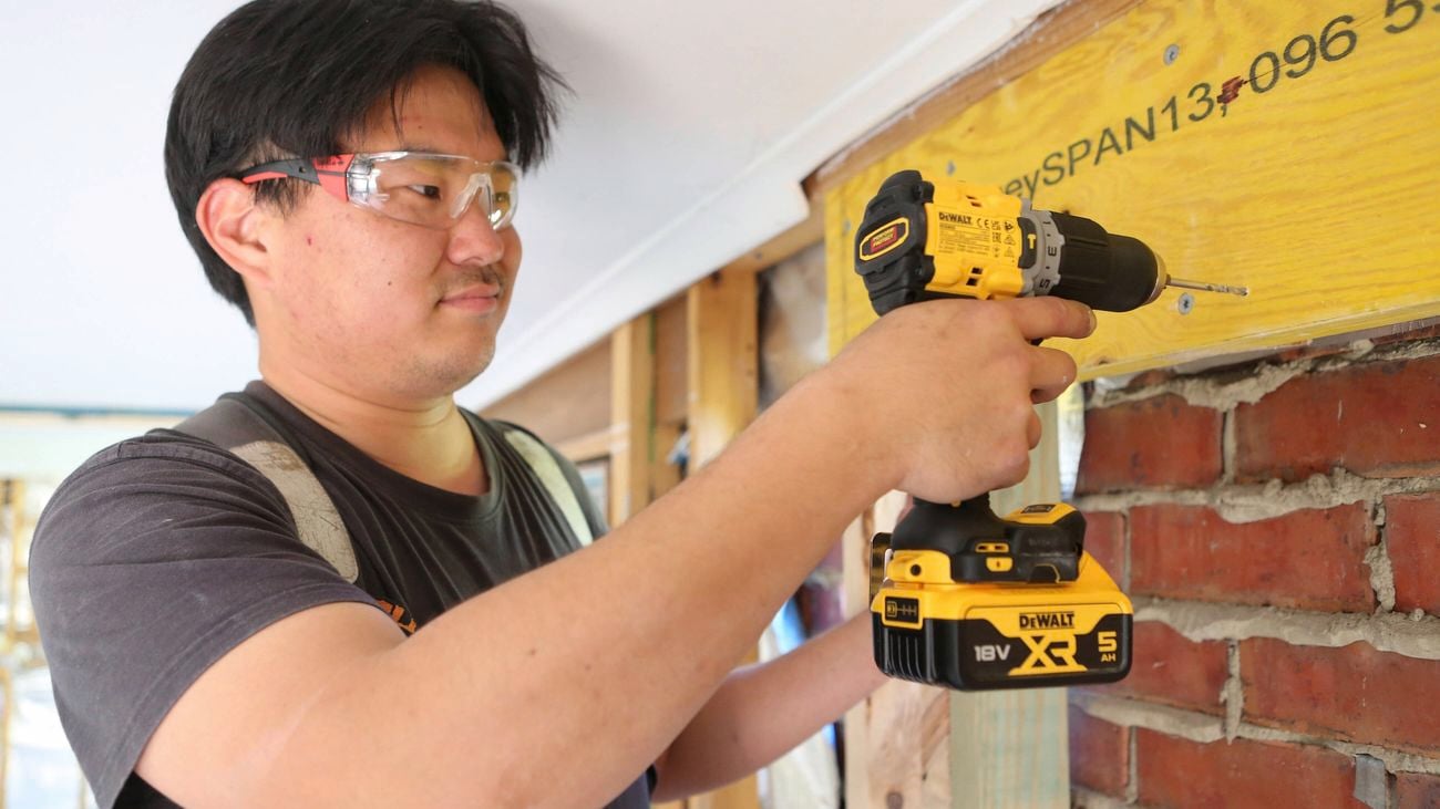 A close up image of a tradesperson wearing safety glasses and using a DeWALT drill.