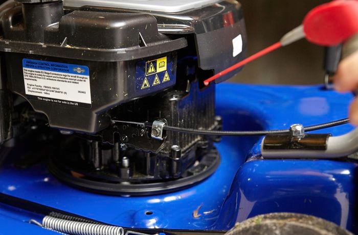 A person applying lubricant to the throttle cable of a lawn mower 