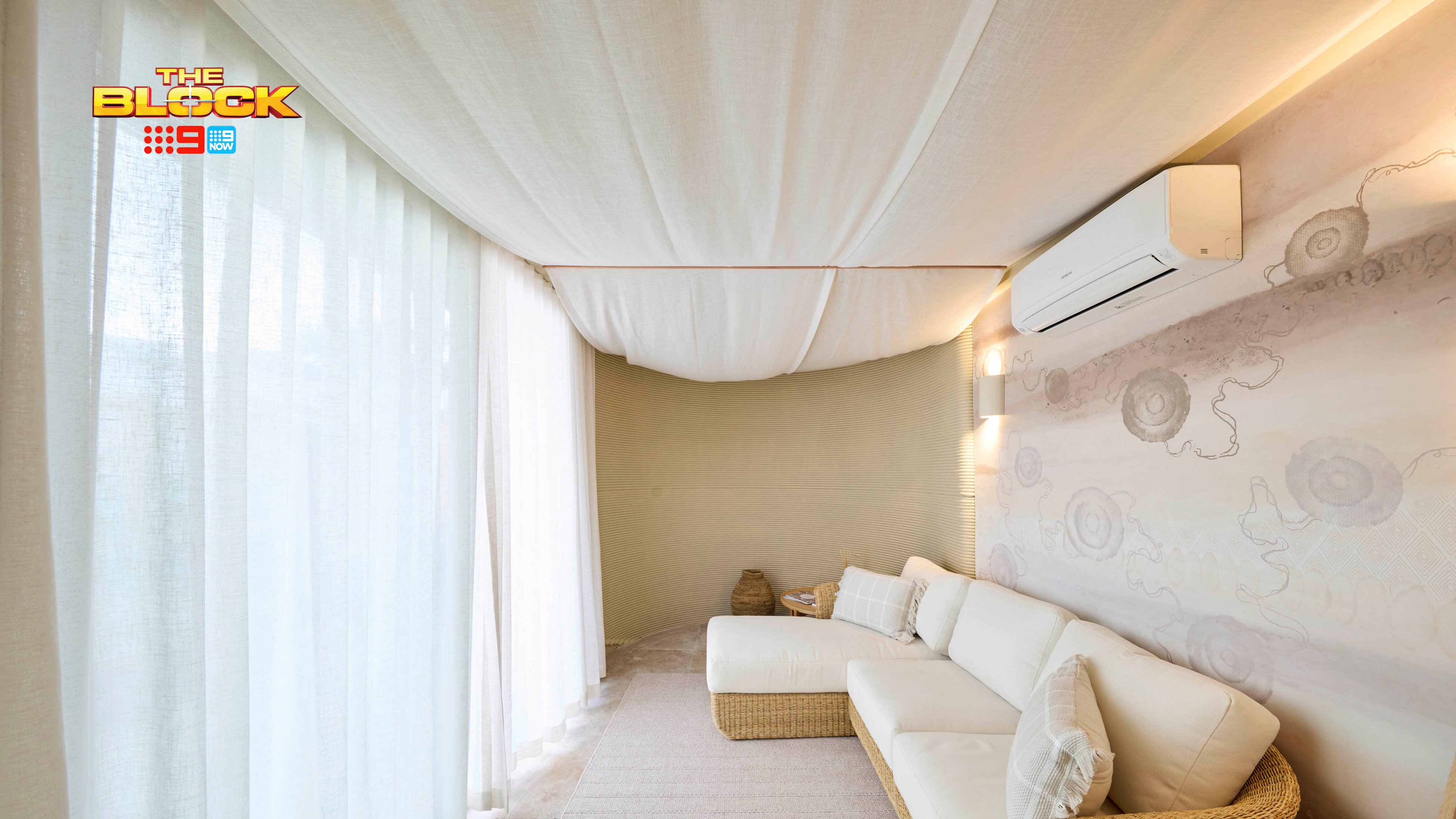 A room with white curtains, a cane lounge and a split system attached to the wall in it.