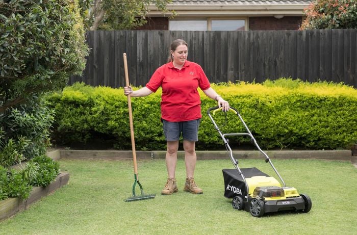  Bunnings team member is holding a dethatching rake in one hand and a brushless cordless scarifier in the other