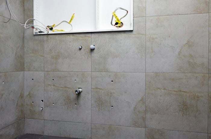 A tiled bathroom wall with holes drilled and pipes capped off
