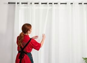 A Bunnings employee arranging sheer curtains on a black curtain rod