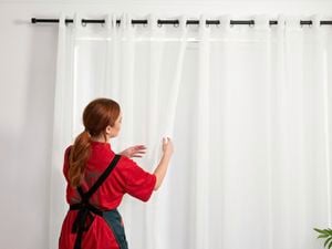A Bunnings employee arranging sheer curtains on a black curtain rod