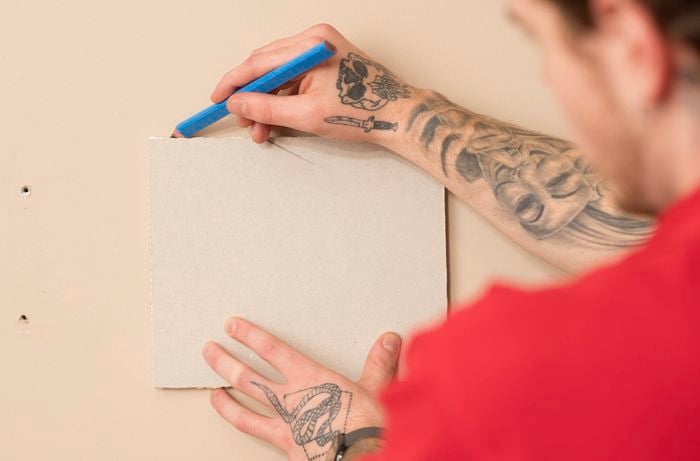 A person with tattoo on both hands is the marking the outline of the plaster cutting onto the wall