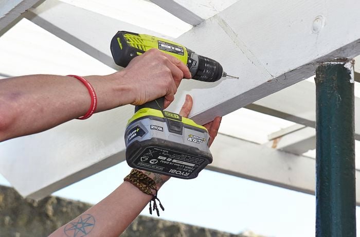 A person drilling into a beam on a pergola