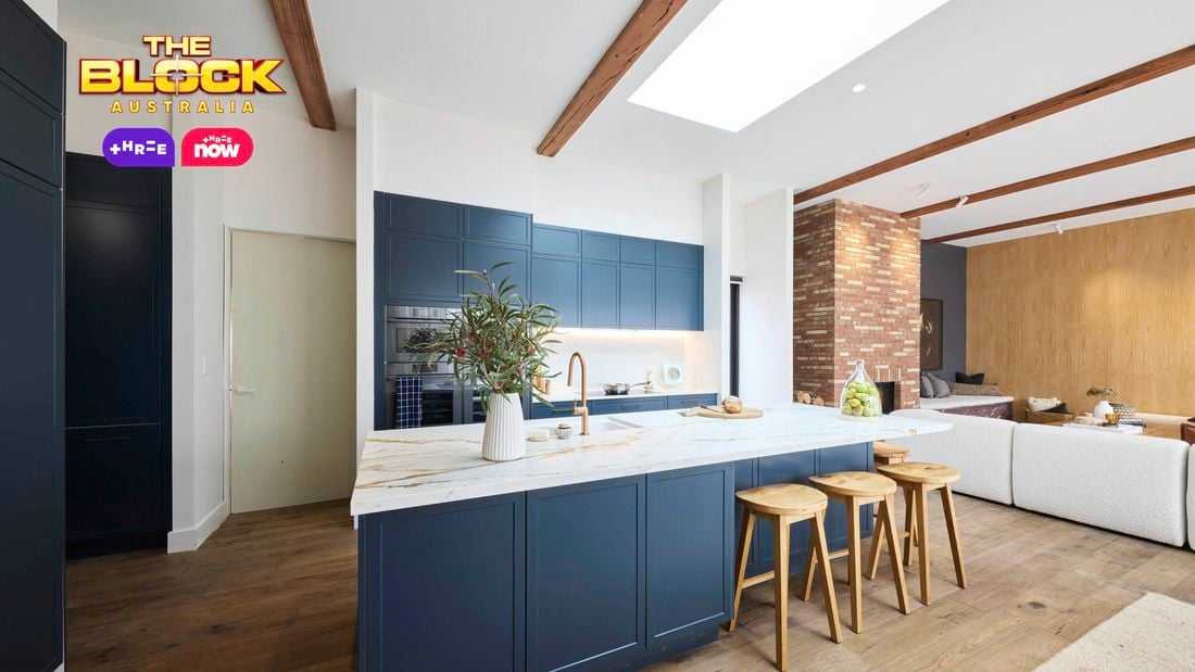 Kitchen with navy island, marble top, wooden stools, and open-plan living.