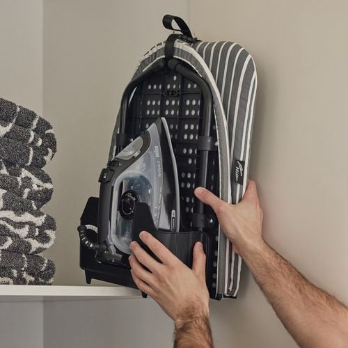 Man putting the folded Hills Tabletop Ironing Board away in a cupboard.