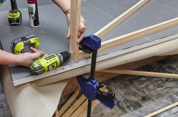 Clamp holding down three lengths of timber while a person drills them together.