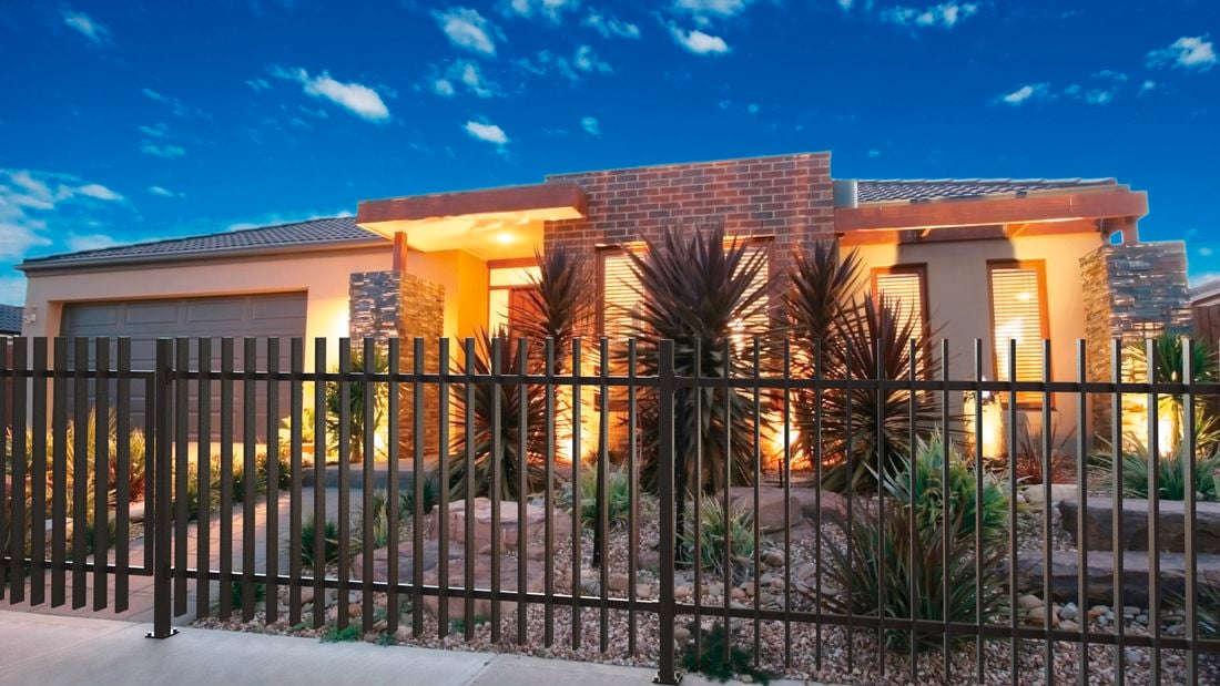 Grey fence sits in the front yard of a house, with outside lights on