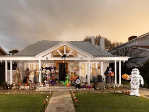 A white house decorated for Halloween with inflatables, pumpkins, skeletons, and themed figures on the porch and front yard.
