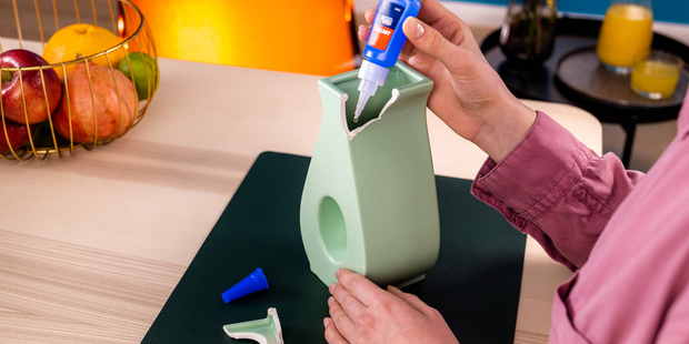 Applying adhesive to a broken ceramic vase during a household repair project.