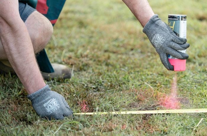 A Bunnings team member using a tape measure and spray paint to mark out positions of holes to dig