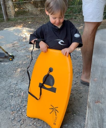 Toddler holding a small orange Summer vibes bodyboard with wrist leash.