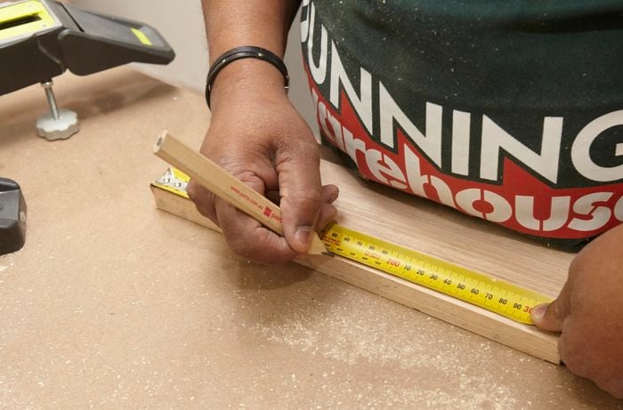 Person using measuring tape and pencil to mark up piece of ply wood.