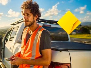 A man with orange vest standing in front of a car and a Commbank logo overlay.