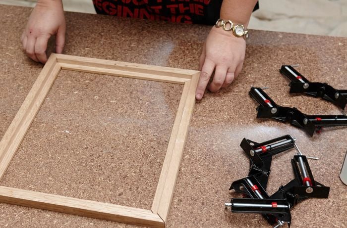 Four panes of a picture frame laid out on a workbench, next to a series of corner clamps