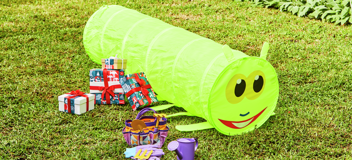 A kids play tunnel is out on the grass with a kids gardening set.