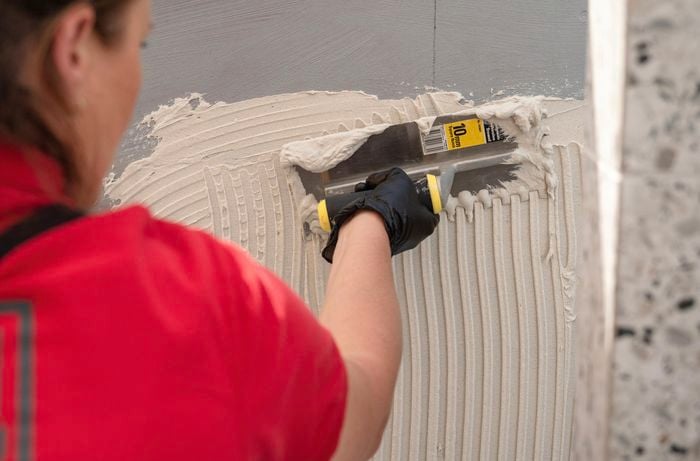 Applying tile adhesive to the wall.