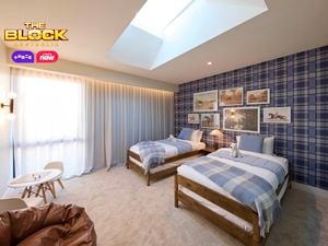 Blue bedroom with a check wallpapered wall and twin beds with blue linens. Opposite is a brown leather bean bag and small kids table. Above the beds are various horse artworks arranged sporadically.
