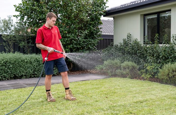 A Bunnings Team Member is watering freshly laid turf in a garden using a hose. 