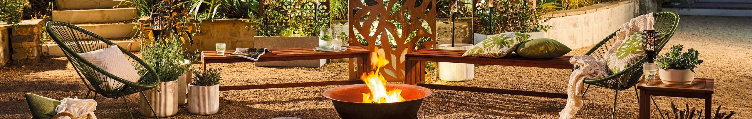 Fire pit, chairs, hanging lights and plants in a backyard