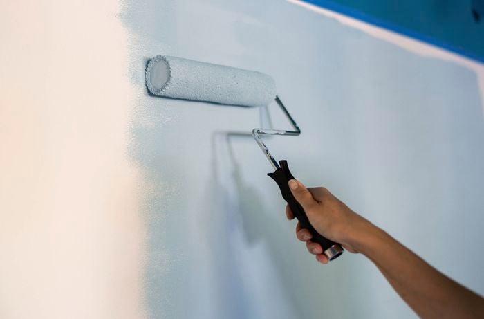 A person using a paint roller to cover the remaining section of the wall with light blue paint. 