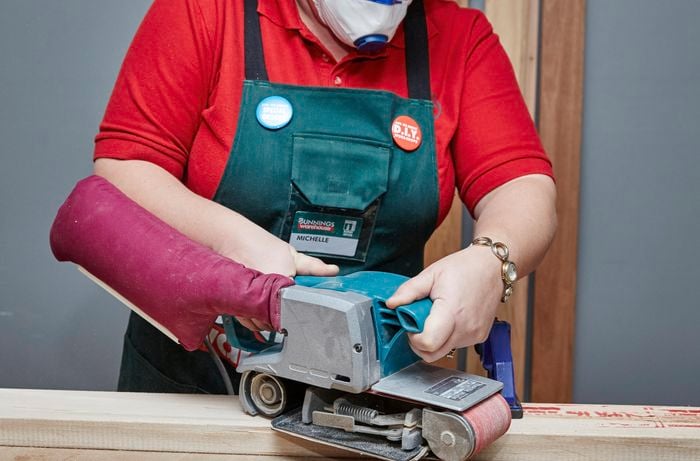 Person using a power sander on bit of timber.