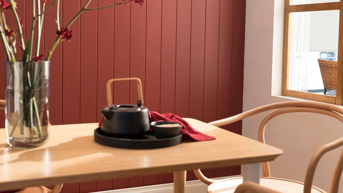 A teapot and vase of flowers on a table in front of a wall painted dark red