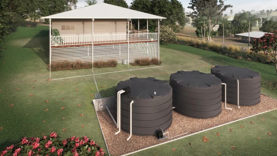 Three round water tanks in the backyard on land with surrounding trees and the back of a house.
