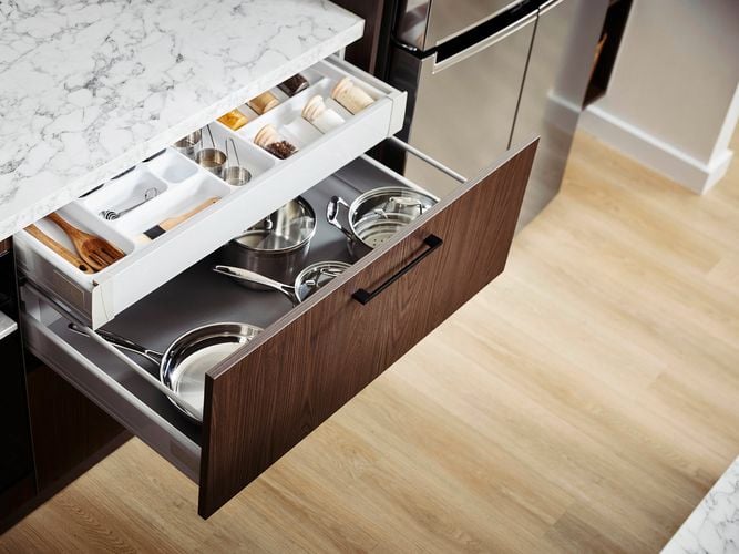 Two Kitchen drawers with crockery in it under a marble benchtop, next to a fridge and an oven.
