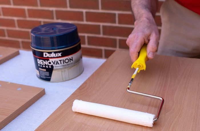 A person is using a paint roller to apply primer to coat the surfaces with a laminate primer