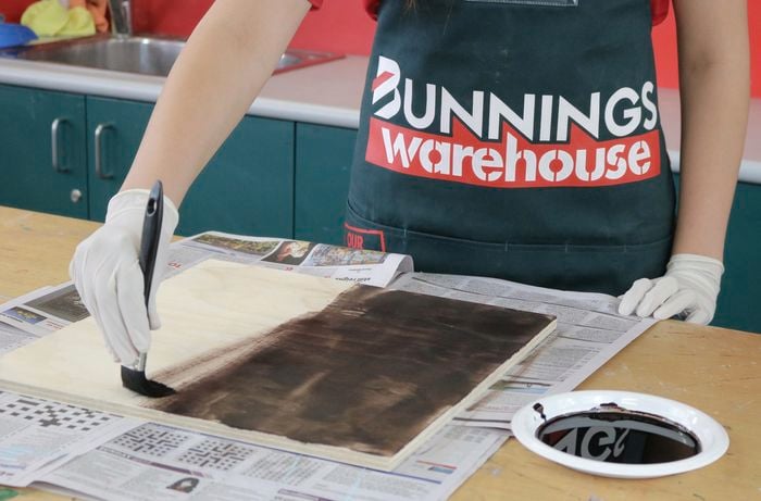 Person staining a sheet of plywood