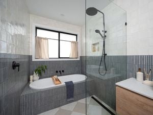 A modern bathroom with grey tiles on the walls, a shower, bath and basin in it