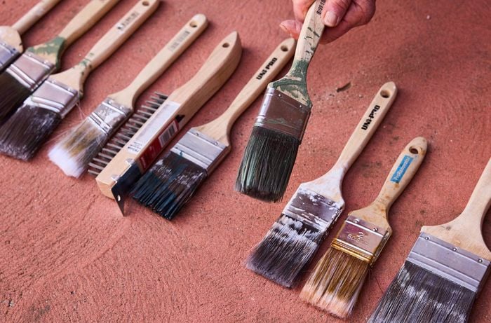 Variety of paint brushes are laid on a red surface