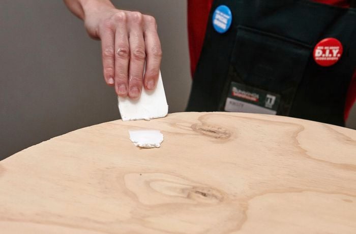 A person filling a hole in a round sheet of plywood using wood filler