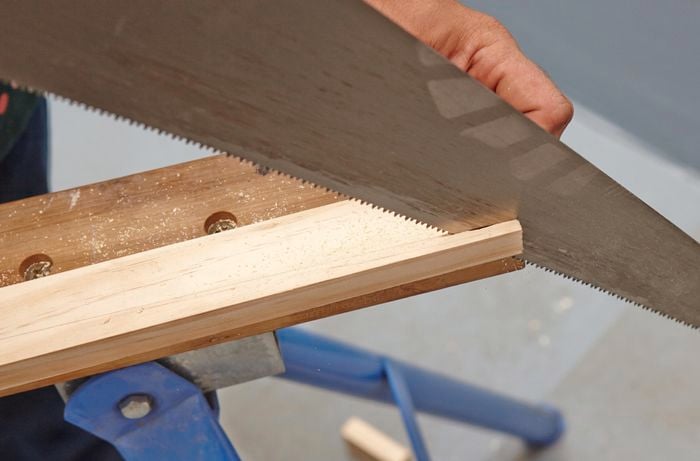 A person sawing down the length of a piece of timber using a hand saw