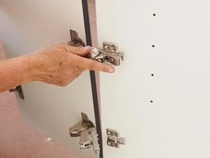 A cabinet door and hinge being affixed to a cabinet