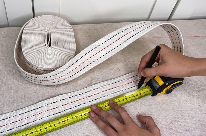 A hand marks webbing to length using a tape measure and marker pen.