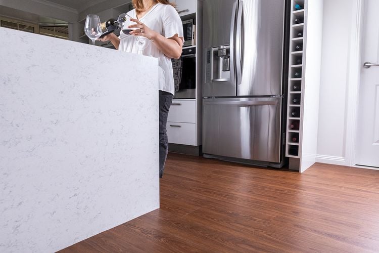 Woman standing in a kitchen with a vinyl plank timber-look floor pouring a glass of red wine