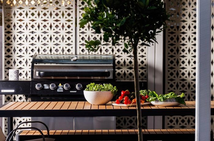 A barbecue machine, dining bench and a table with fruits and vegetables.