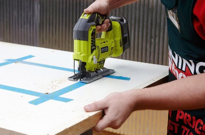 A person cutting a hole in a door using a jigsaw